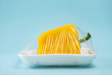 Sarı dolmalık biber mavi arka planda plastik streç film sarılı. Geri dönüşüm ve çevre kavramı: taze gıda Plastik paket