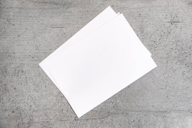 Boş kağıt sayfalarının gri arka plan üzerinde. Beyaz Çimento stilize masa üstü üzerinde döşeme kağıt üstten görünüm