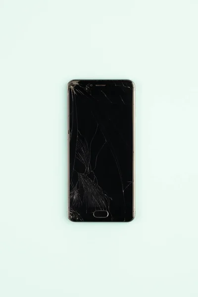 Mobile phone with broken black screen, top view. Distressed damaged smartphone in pale green background, vertical shot