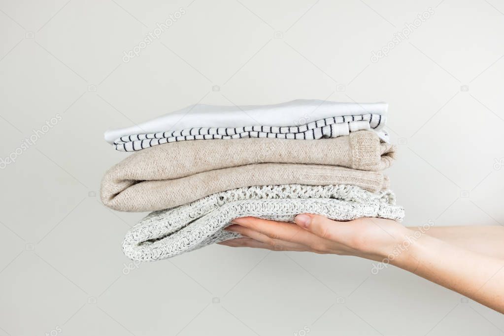 Heap of clothes in female hands. Neatly stacked simple clothing at white background