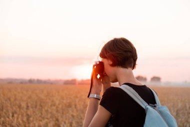 Arkadan aydınlatmalı parlak'nde Günbatımı Fotoğraf çekme bir kadın figürü. Akşam güneş ışığı alan, ayakta ve vintage analog kamera kullanarak kadın kişi