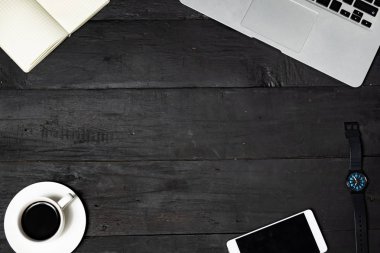 İş yeri düz siyah arka plan üzerinde yatıyordu. Dizüstü bilgisayar, not defteri, kahve ve cep telefonu eksikliği ahşap doku, üstten görünüm