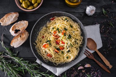 Bir İtalyan makarna, üstten görünüm pişmiş pan. Düz geleneksel spagetti yemek sebze, sarımsak ve zeytin rustik siyah arka plan üzerine yatırın