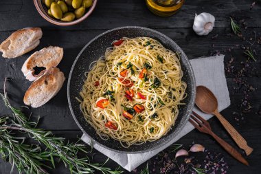 Pan of cooked italian pasta, top view. Flat lay of traditional spaghetti meal with vegetables, garlic and olives on black rustic background clipart