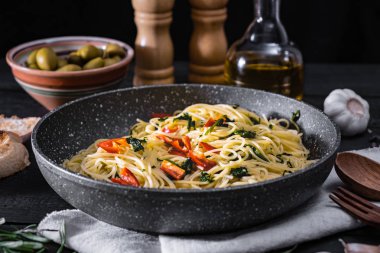 Bir İtalyan makarna pişmiş pan. Geleneksel spagetti yemek sebze ve rustik siyah arka plan üzerine zeytin ile