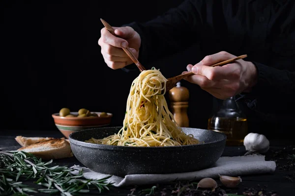 在平底锅上供应传统的意大利面食 用勺子和叉子拿意大利面的雄性手 低调射击 — 图库照片