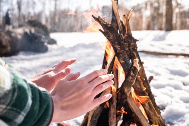 Bir kamp ateşi karlı huş ormandaki yakınındaki tadını çıkarma. Kadın kişi ormanda bir güneşli kış gününde bir ateşin yanında ısınmaya