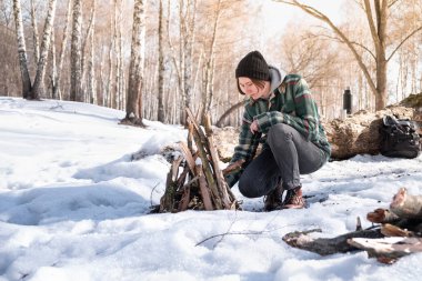 Bir kamp ateşi karlı huş ağacı ormanda yapma. Kadın kişi ormanda bir güneşli kış gününde bir ateş yakın