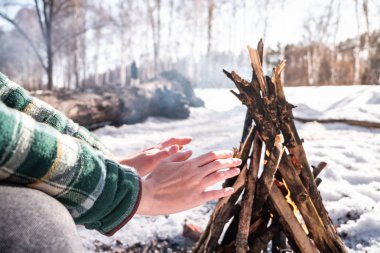 Bir kamp ateşi karlı huş ormandaki yakınındaki tadını çıkarma. Kadın kişi ormanda bir güneşli kış gününde bir ateşin yanında ısınmaya