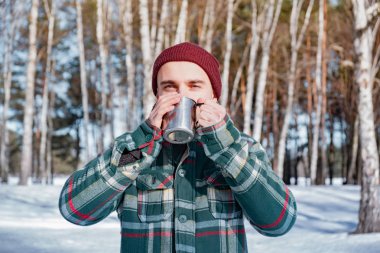 Karlı kış orman bir kaba erkek kişi içecekler. Kareli gömlekli adam açık havada kahve tutar