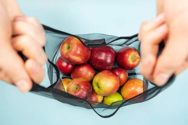 Holding a reusable string bag full of apples. Sustainable eco packaging concept: shopping for groceries with a multi-use bag to reduce ecological footprint