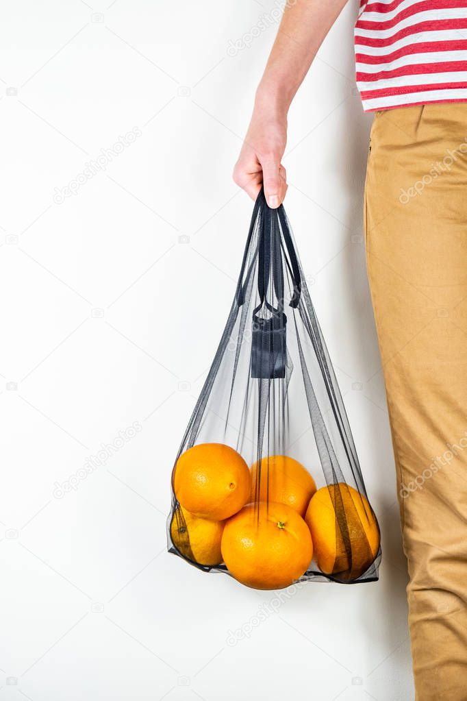 Holding a reusable string bag full of oranges. Sustainable eco packaging concept: shopping for groceries with a multi-use bag to reduce ecological footprint