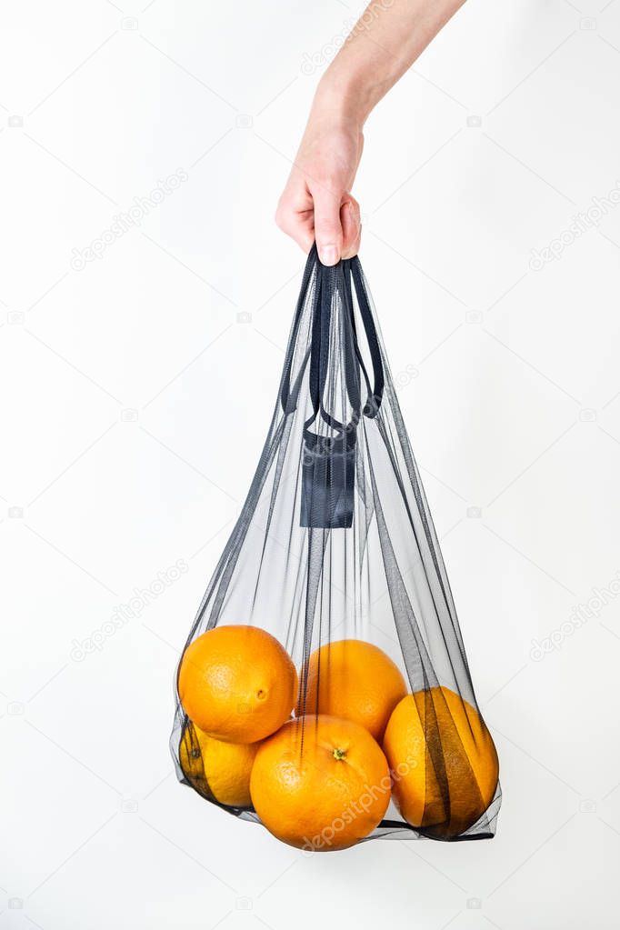 Holding a reusable string bag full of oranges. Sustainable eco packaging concept: shopping for groceries with a multi-use bag to reduce ecological footprint