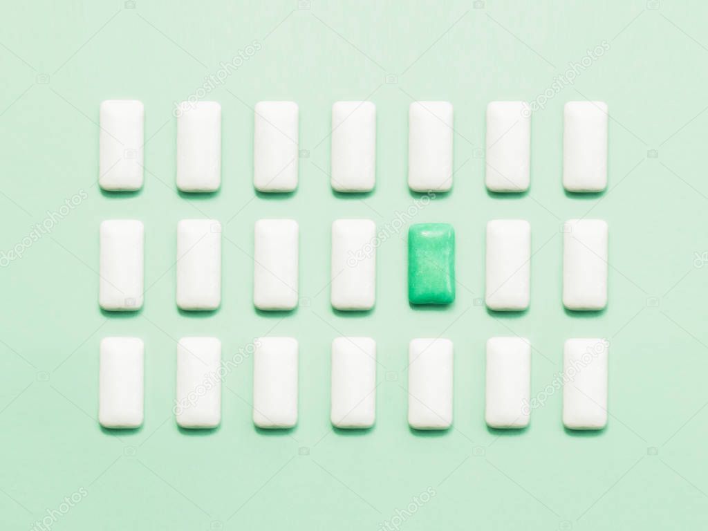 One green chewing gum  standing out of white chewing gums