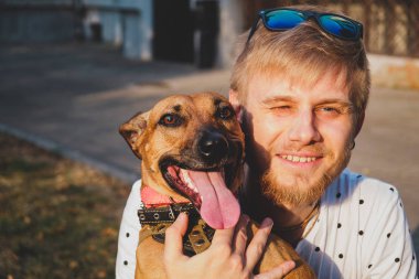 Insan ve köpek dostluk: genç adam açık havada köpeğini kucaklar