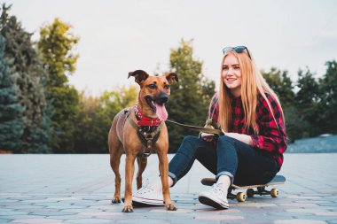 Genç patenci kız şehirde köpeği ile eğleniyor.