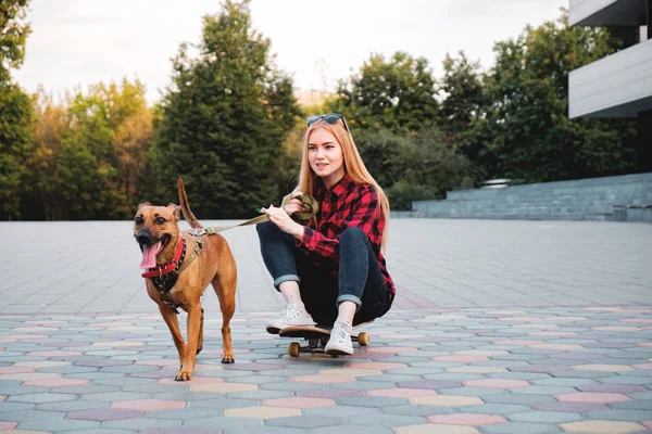 Adolescente skater chica divirtiéndose con su perro en la ciudad . — Foto de Stock