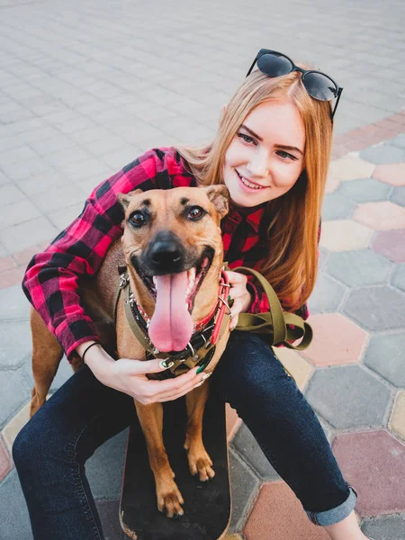 Joven mujer se sienta en un monopatín con su querida mascota . — Foto de Stock