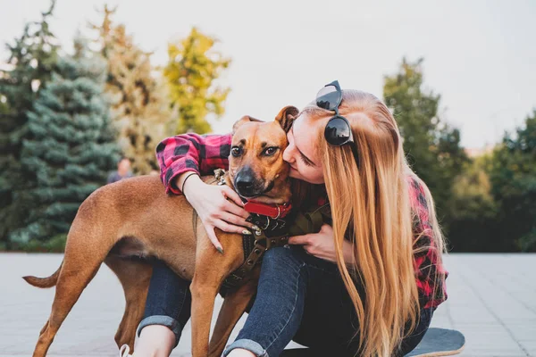 Chica patinadora adolescente besando a su perro en el entorno urbano . — Foto de Stock