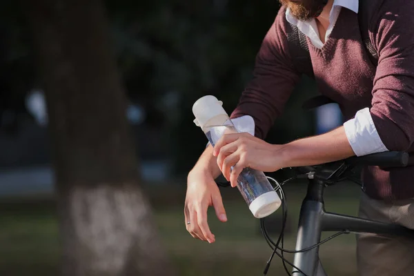 Water bottle in the hands of a bicycle commuter. Staying hydrated, active urban lifestyle, using a bike in the city