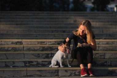 Kadın köpeğinin yanına oturur, doğal güneş ışığı, şehir manzarası. Şehirdeki evcil hayvanlarla yaşam tarzı, yumuşak tilki teriyeri.
