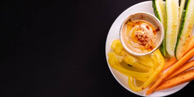 Humus sosu ve sebzeler tabakta, fotokopi alanı olan üst manzara. Sağlıklı vejetaryen yemeği veya aperatif, bitki bazlı ve vitamin açısından zengin yiyecekler.