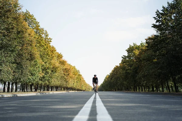 Man rides a gravel bike in the middle lane of the road. Well equipped cyclist on a modern bicycle outdoors, symmetric image