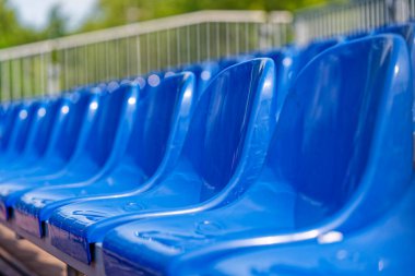 Mavi plastik koltuklar durmaksızın sıralanır. Üniformalı ve temiz. Basit biçimler terasta yavaşça kıvrılır, izleyiciler için ayarlanır ve bir sonraki oyundan önce sessizlik.