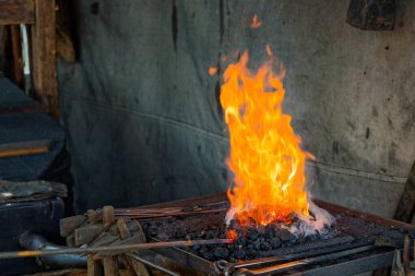 Parlayan kömürle dolu metal bir ocak beton bir duvarın yanında kükrer. Uzun saplı çekiçler menzilde asılı durur ve kızgın ateş yatağının üzerinde titreşen ısı yoğun bir demirde demiri şekillendirmeye hazırdır..