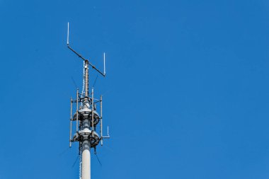 Açık mavi bir gökyüzü uzun bir direği çerçeveler. Dairesel ve uzun radyo antenleri farklı yönleri gösteriyor. Direk boyunca sağlam kollara sabitlenmiş. Parlak gün, temiz ve açık bir teknik sahne sunar..