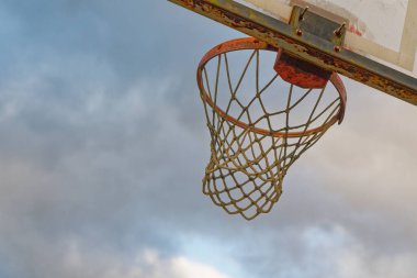 Yıpranmış bir basketbol potası mavi bulutlu bir gökyüzüne karşı duruyor. Kırmızı kenar ve çerçeve lekeli ve paslı, sedye küçük bir kalp izi taşıyor. Yaş ve toz saraydaki metali sertleştiriyor..