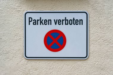 Metal levhada park cezası ve kırmızı yuvarlak bir işaret var. Durmak yok, park etmek yok. Plaka çitin yanında duruyor, küçük bir avludaki sürücüler için açık bir uyarı..