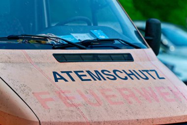 Beyaz servis arabası, yıpranmış Atom Schutz Feuerwehr metni ve silinmiş çıkartmaları gösteriyor. Sıkıcı boya ve toz, eski bir filo görüntüsünü iletir. Editör ve belgesel temaları için uygundur..