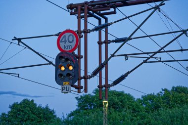 Askıya alınmış bir demiryolu sinyali hız limiti olan 40 kmh 'lik sabit sarı bir yön gösteriyor. Birlik rayların üzerinde çelik bir kirişin üzerinde oturuyor. Danimarka 'nın Padborg şehrinde kablolar gökyüzünde dönüyor..