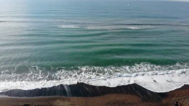 Zümrüt renkli su ve beyaz köpükle kıyıya vuran hava manzaralı okyanus dalgaları.