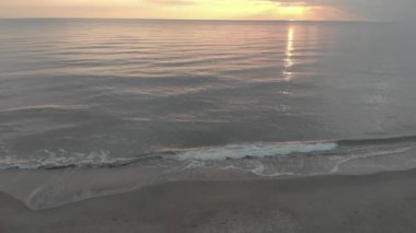 Okyanusun üzerinde gün batımında, uzun dalgalar sahile çarpıyor ve sarı ışık bulutlar ve rahatlatıcı atmosfer arasında yayılıyor.