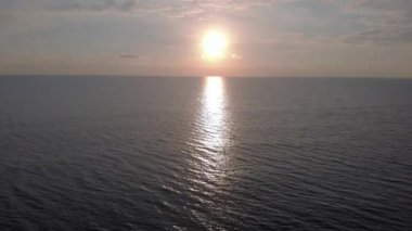 Okyanusun üzerinde gün batımı yeşil zümrüt renkli yüzey suyu ve bulutlar tarafından karartılmış güneş ışığı ile su ve bulutlu gümüş gökyüzü üzerinde.