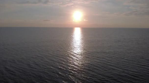 Coucher de soleil au-dessus de l'océan avec une eau de surface ondulée de couleur émeraude verte et un soleil obscurci par des nuages avec son beau rayon de soleil sur l'eau et un ciel argenté nuageux