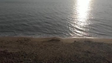 Güneş batarken kumsaldan okyanusa uçun. Yeşil zümrüt renginde yüzey suyu ve okyanus dalgaları kıyıya vuruyor. Güneş ışığı suya vuruyor.