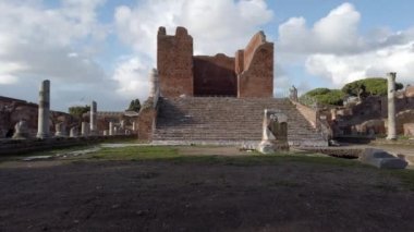 Pan, Ostia Antica 'nın arkeolojik kazılarında Capitolium kalıntıları ile Roma harabeleri, sütunları ve heykelleri ve mermer levrek kabartmaları ile çevrili.