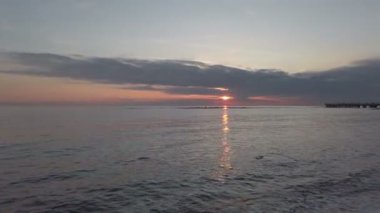 Pastel renkli gökyüzü ile deniz üzerinde gün batımında, dalgalar arasında bir karabatak balıklar