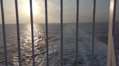 Okyanusun üzerinde gün batımını izlemek ve çelik parmaklıklar arasındaki denizi yansıtmak ve değişim umuduyla birinci şahıs 4K atışı.