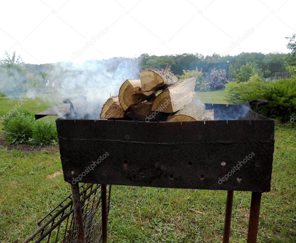 Beautiful red fire from slice wood, dark grey black coals inside metal brazier. Wood burning in the brazier on bright yellow fire. Flames fires preparation for cooking barbecue. Brazier on nature bbq.