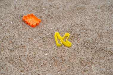 Sıcak ve güneşli bir günde, bir çift parlak sarı parmak arası terlik kumlu bir plajda dinlenir, güneş ışınlarını emer.