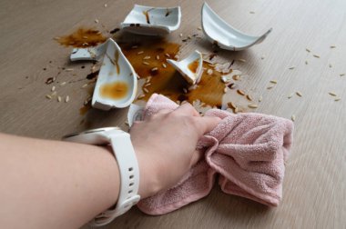 Bir el, ahşap bir masa yüzeyindeki birkaç kırık tabakla birlikte dağınık bir sos dökülmesini özenle temizliyor.