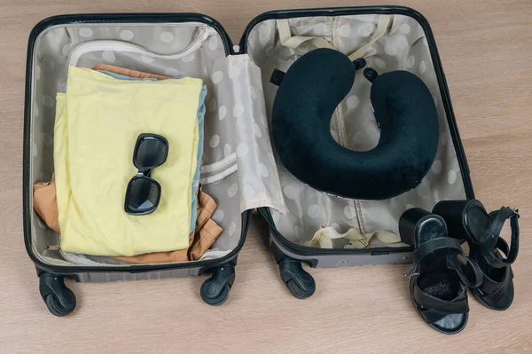 A colorful suitcase packed with clothing, sunglasses, a neck pillow, and sandals for an exciting journey