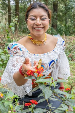 Otavalo, Ekvador - 6 Ağustos 2025: Geleneksel giyinmiş yerli kadın, Lantana Camara çiçeklerine tünemiş Patricia dercyllidas kelebeğini tasarlıyor, doğal bir şekilde..