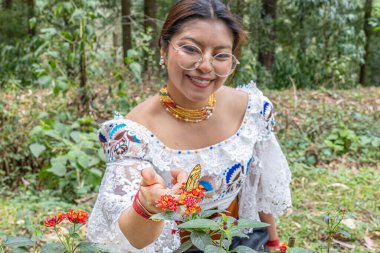 Otavalo, Ekvador - 6 Ağustos 2025: Geleneksel giyinmiş yerli kadın, Lantana Camara çiçeklerine tünemiş Patricia dercyllidas kelebeğini tasarlıyor, doğal bir şekilde..