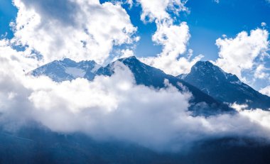 Mavi gökyüzü ve beyaz bulutlar dağların yüksek karlı zirveleri