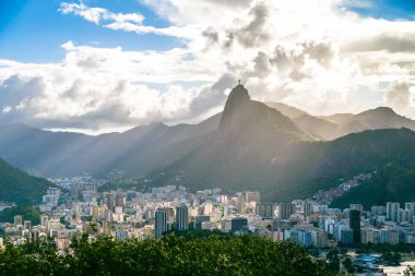 Cityscape yüksek dağlar, binalar ve beyaz bulutların üstünde mavi gökyüzü ile güneş ışınları ile
